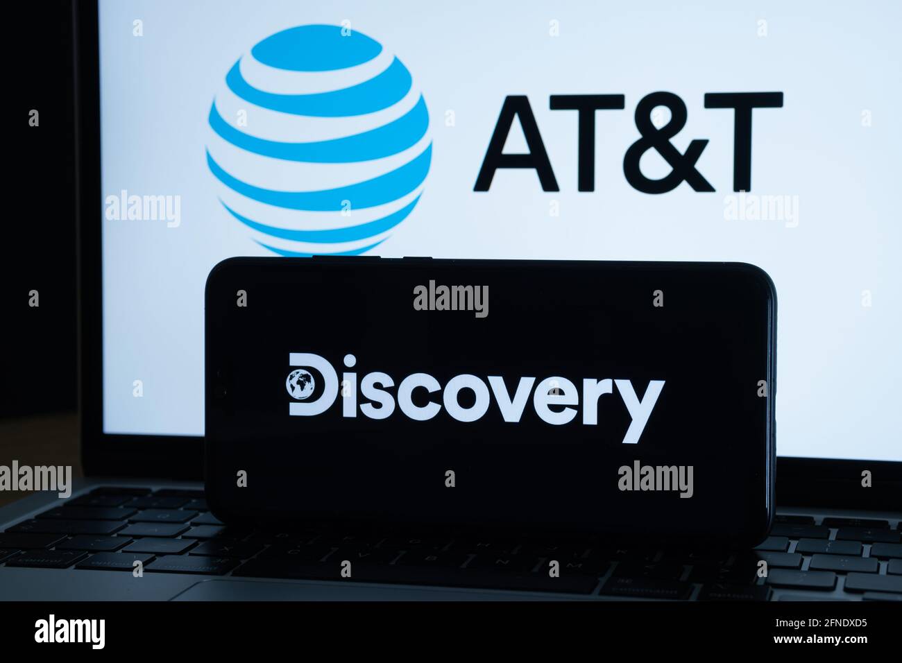 Concetto di fusione di Discovery e AT&T. Logo Discovery visualizzato sullo smartphone scuro e LOGO AT&T sullo schermo del notebook sfocato sul retro. Staffor, Re Unito Foto Stock