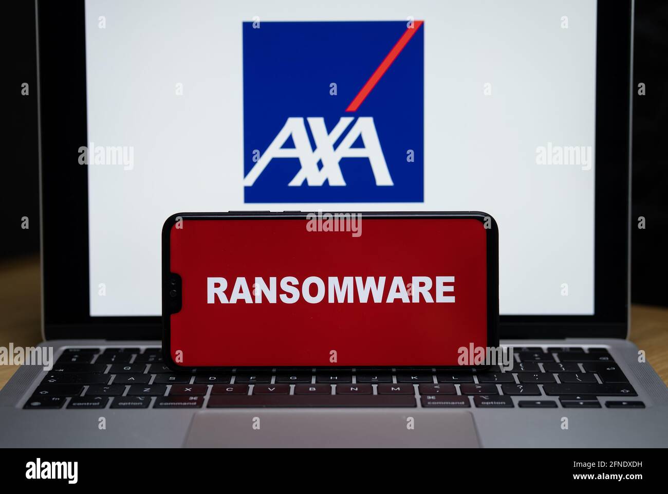 Logo AXA sullo sfondo sfocato e parola RANSOMWARE sullo smartphone di fronte. Stafford, Regno Unito, 16 maggio 2021. Foto Stock