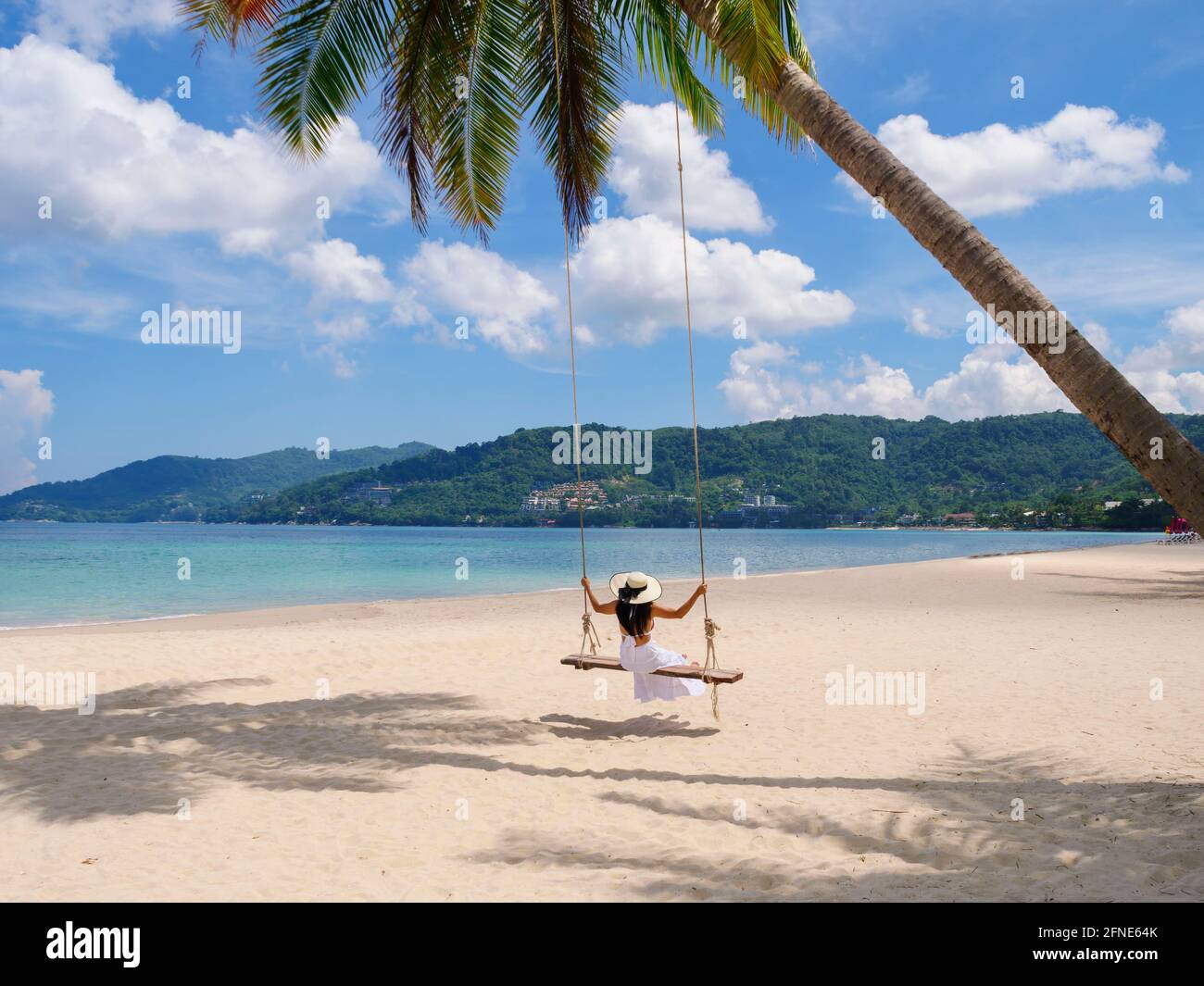 Phuket, Thailandia. Paradiso tropicale sulla spiaggia con altalena con ragazza in camicia bianca. Le donne si rilassano sull'altalena sotto la palma di cocco alla bella tropica Foto Stock