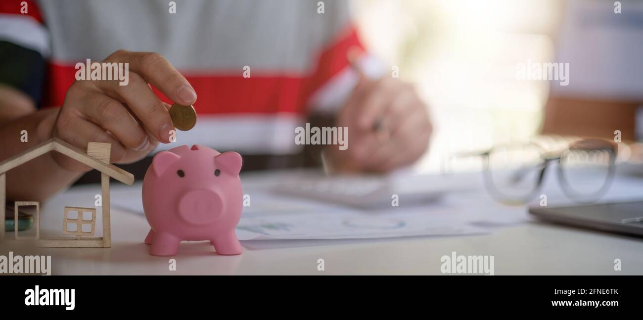 Primo piano di uomo che mette le monete in una banca piggy e calcolando con calcolatore per soldi di risparmio e concetto di prestito domestico finanziario. Foto Stock