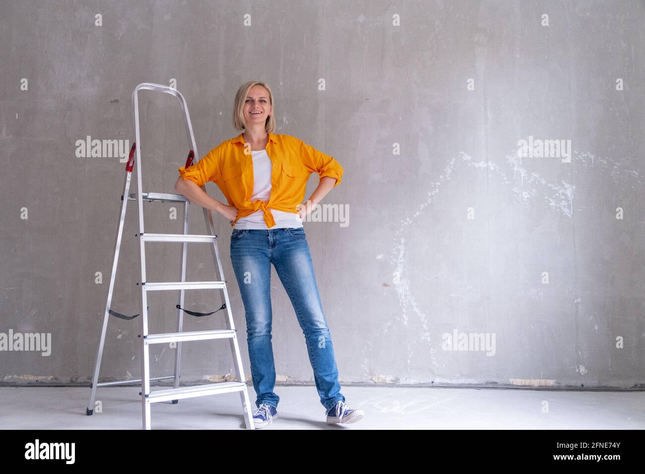 Appartamento di ristrutturazione. Donna felice si siede sulle scale vicino a muro vuoto a casa. Muro libero, ripara casa con le proprie mani. CopySpace per il testo. Foto Stock