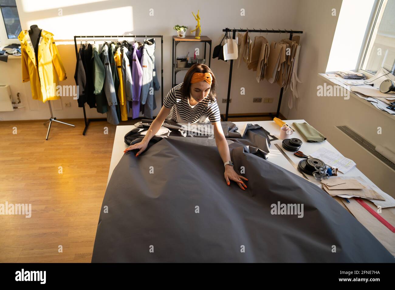 La fogna srotola il tessuto sul tavolo atelier. Stilista di moda su misura in studio di moda lavora su nuovi abiti Foto Stock