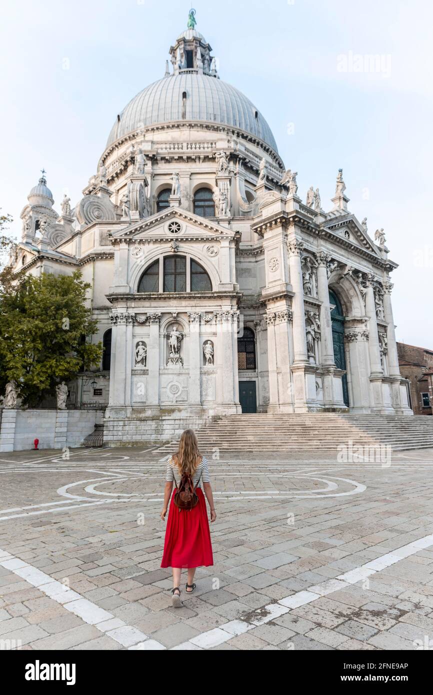 Giovane donna con abito rosso davanti alla chiesa, Basilica di Santa Maria della Salute, Venezia, Veneto, Italia Foto Stock
