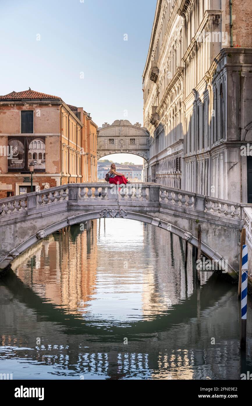 Giovane donna con gonna rossa, turista seduto su una ringhiera ponte, ponte sul Rio di Palazzo, dietro Ponte dei Sospiri, Venezia, Veneto, Italia Foto Stock