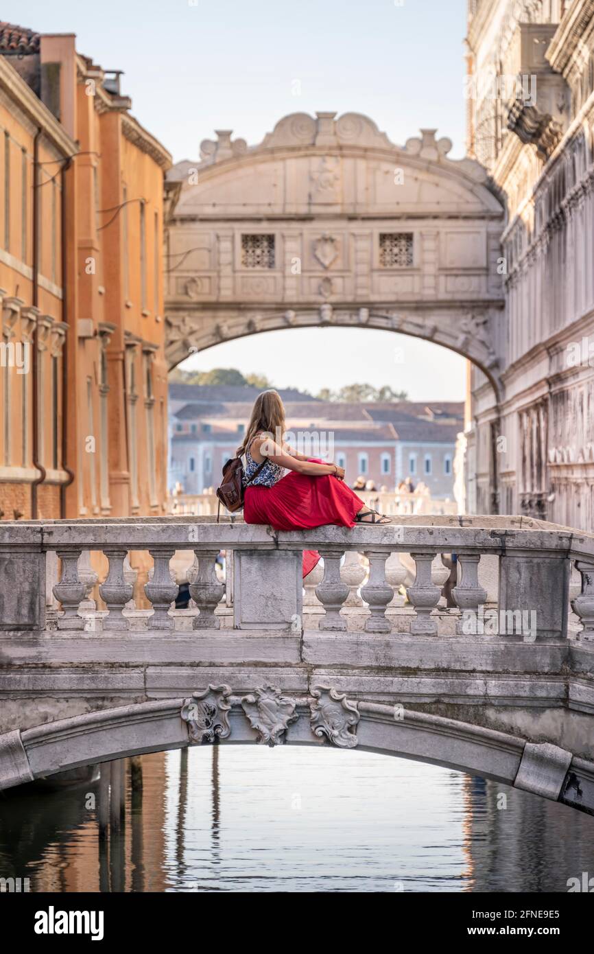 Giovane donna con gonna rossa, turista seduto su una ringhiera ponte, ponte sul Rio di Palazzo, dietro Ponte dei Sospiri, Venezia, Veneto, Italia Foto Stock