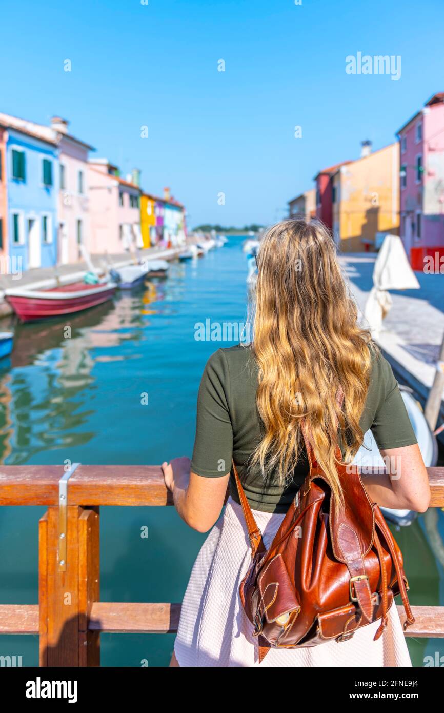 Giovane donna di fronte a case colorate, canale con barche e facciate colorate casa, Burano Island, Venezia, Veneto, Italia Foto Stock