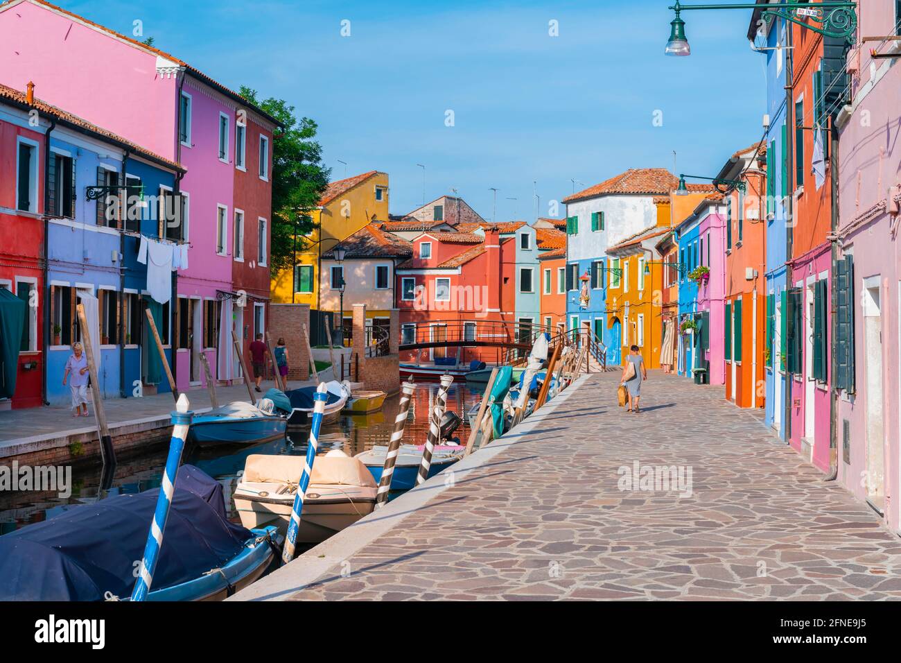 Donna che cammina attraverso case colorate, canale con barche e facciate colorate casa, Burano Island, Venezia, Veneto, Italia Foto Stock