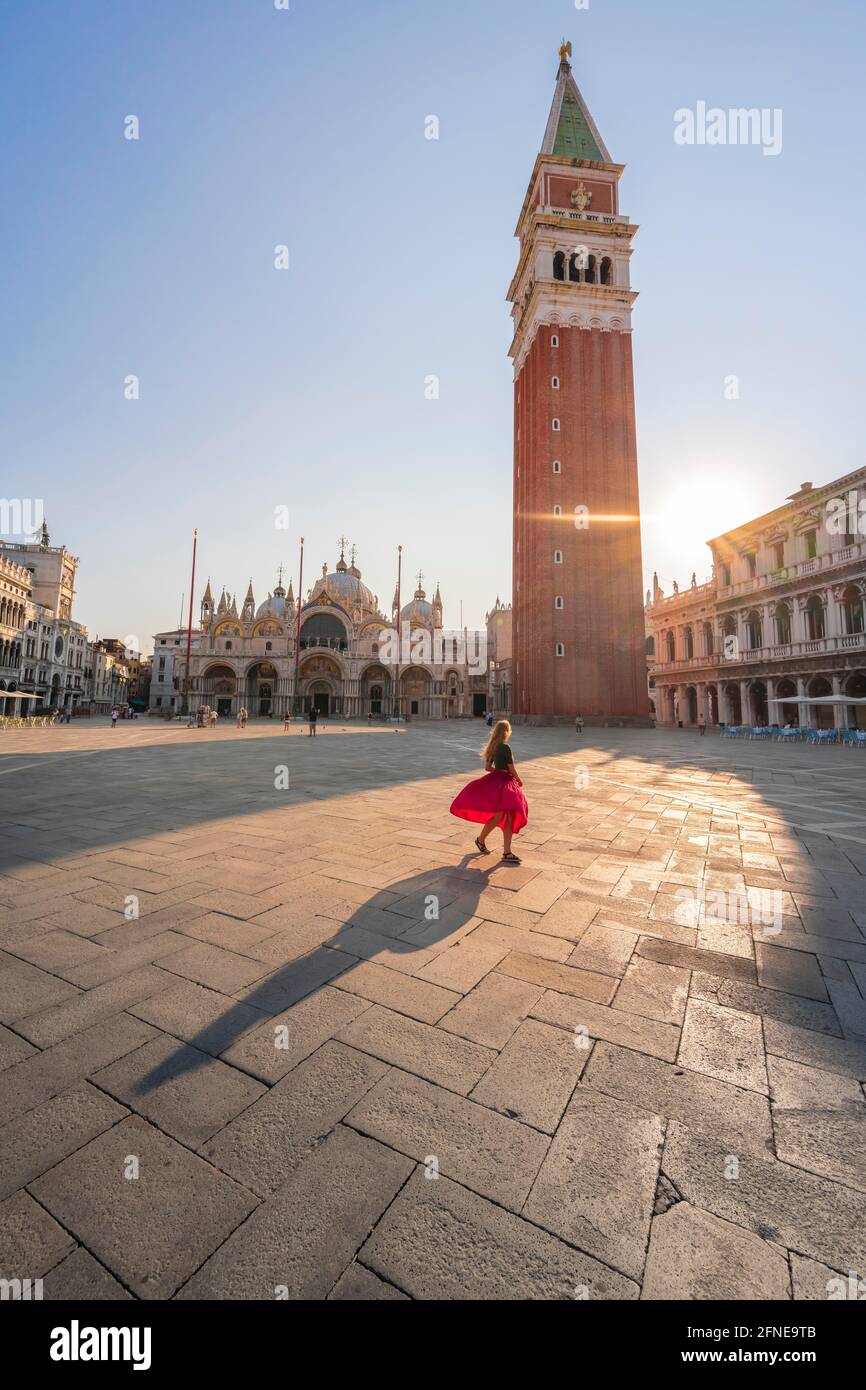 Giovane donna, turistica con abito rosso in Piazza San Marco, il sole splende su Piazza San Marco con il Campanile di San Marco, Venezia, Veneto, Italia Foto Stock