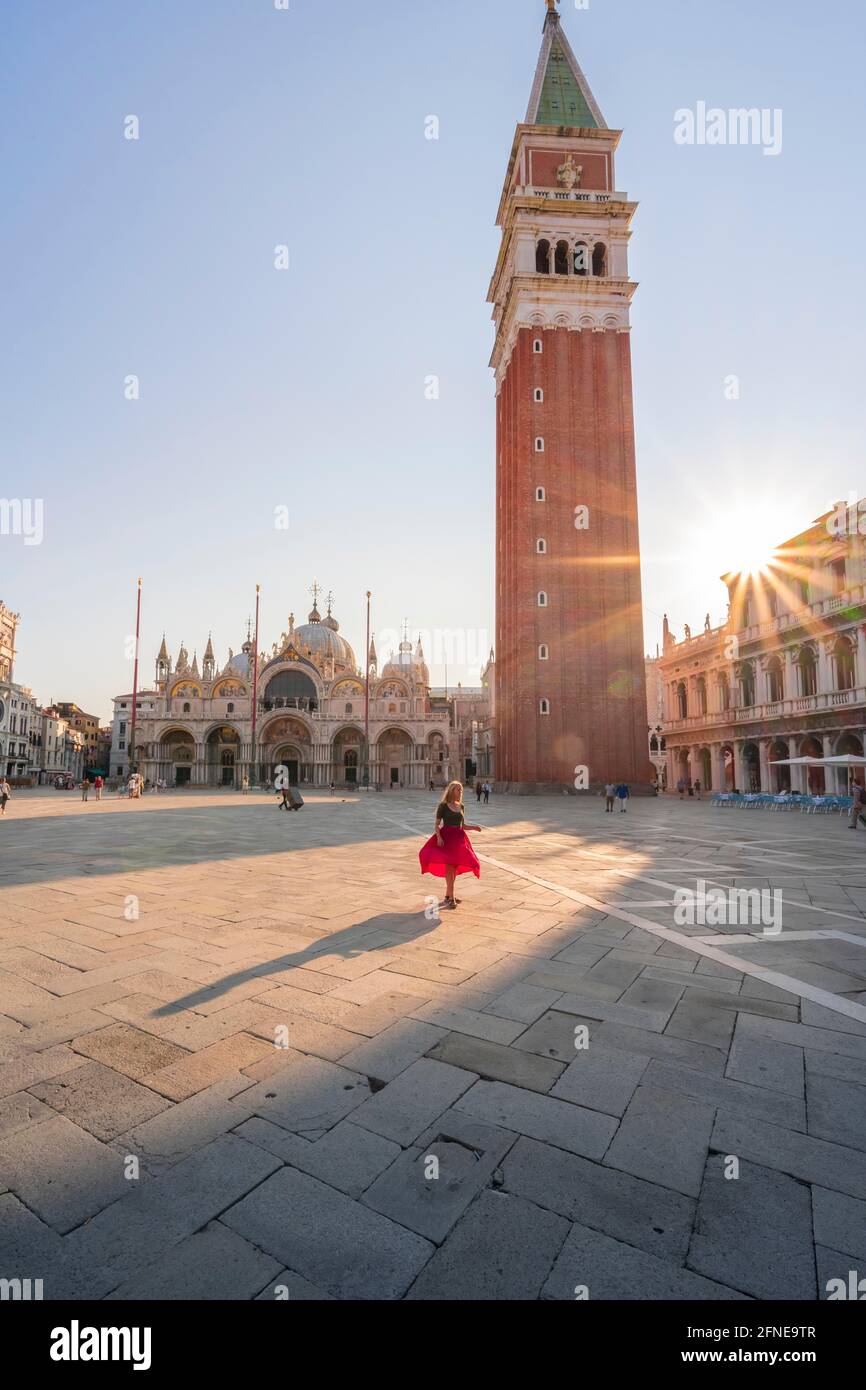 Giovane donna, turistica con abito rosso in Piazza San Marco, il sole splende su Piazza San Marco con il Campanile di San Marco, Venezia, Veneto, Italia Foto Stock