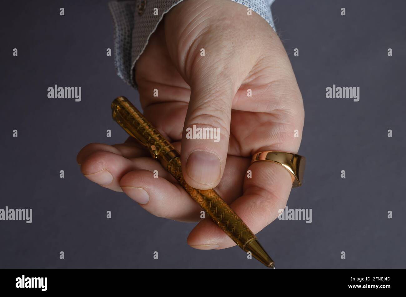 Un uomo con un anello d'oro offre una penna di metallo gialla. Mano  sinistra maschile adulto con un anello di segnalazione sul dito indice.  Sfondo grigio. Vista dall'alto Foto stock - Alamy