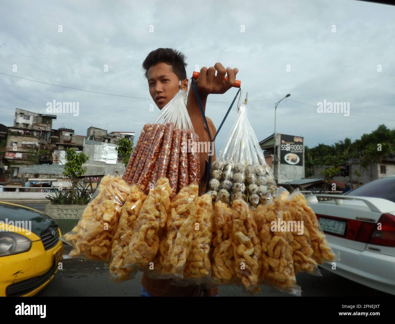 Giovane uomo che vende arachidi e patatine di cotenna di maiale, uova e spuntini ai conducenti di auto su una strada a Novaliches, Manila, Filippine Foto Stock
