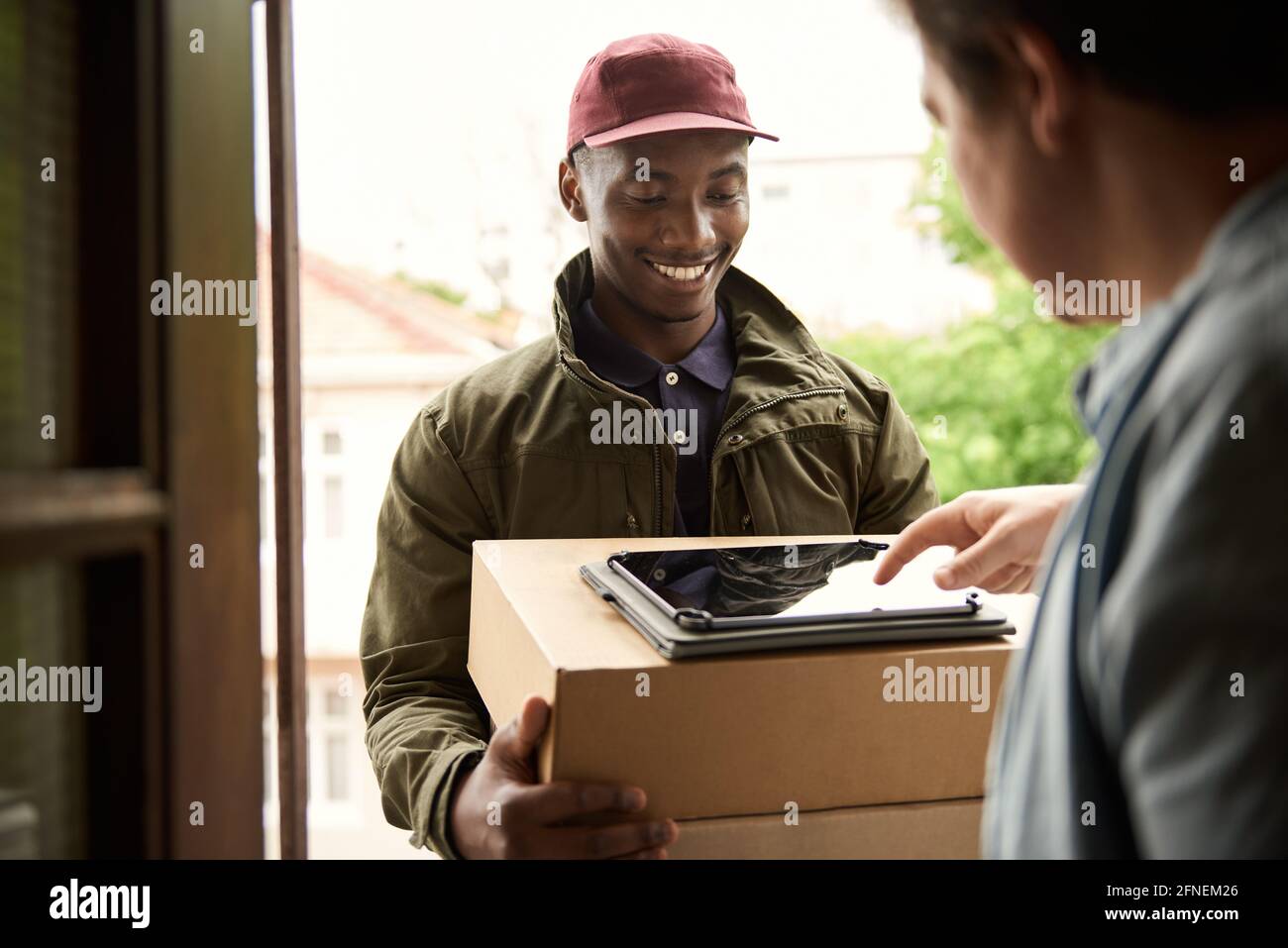 Sorridente corriere africano ottenere la firma digitale di un cliente per un consegna Foto Stock