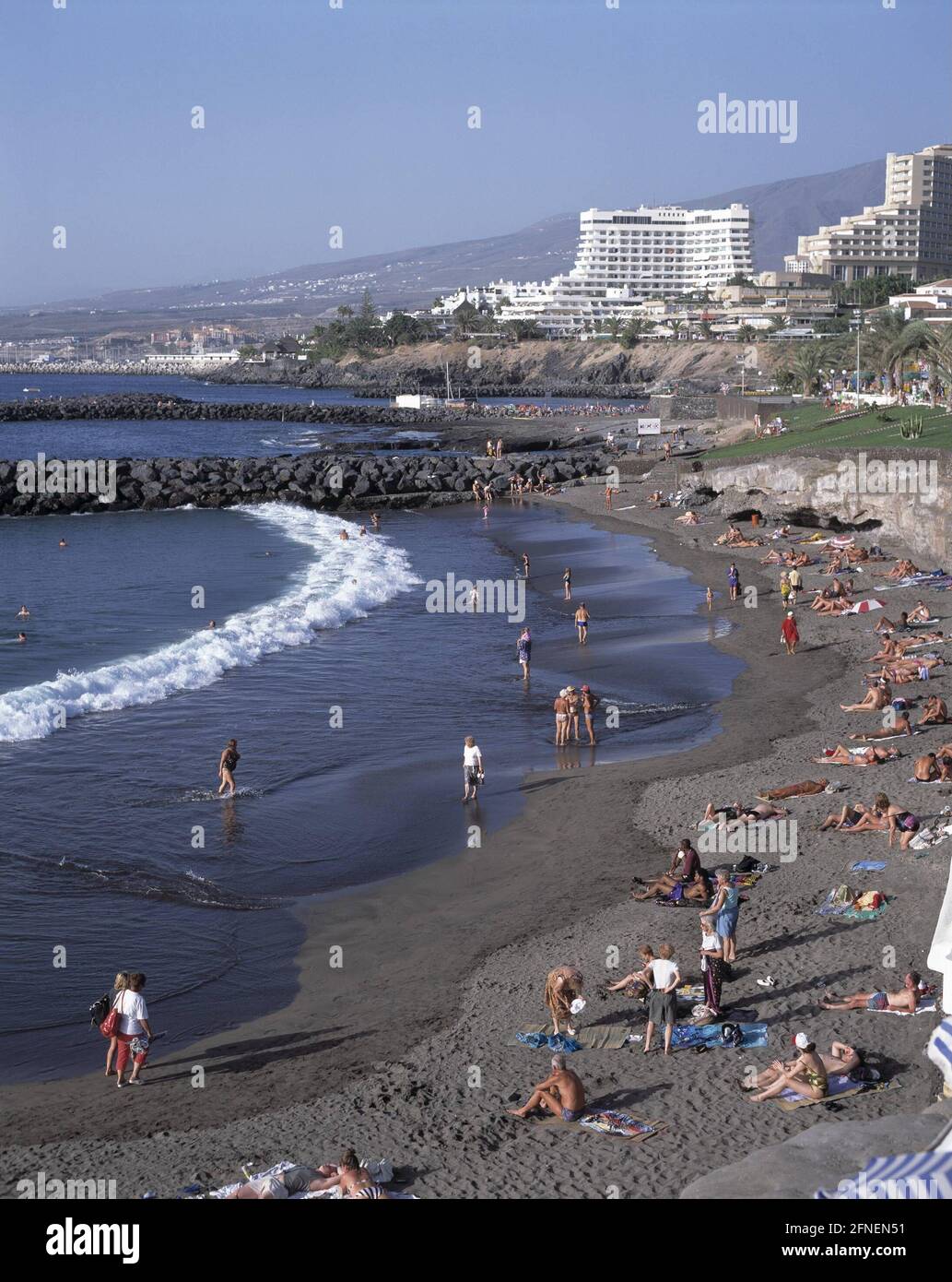 Turisti sulla spiaggia di Playa de las Americas. Sullo sfondo gli alberghi tipici delle Isole Canarie. [traduzione automatizzata] Foto Stock