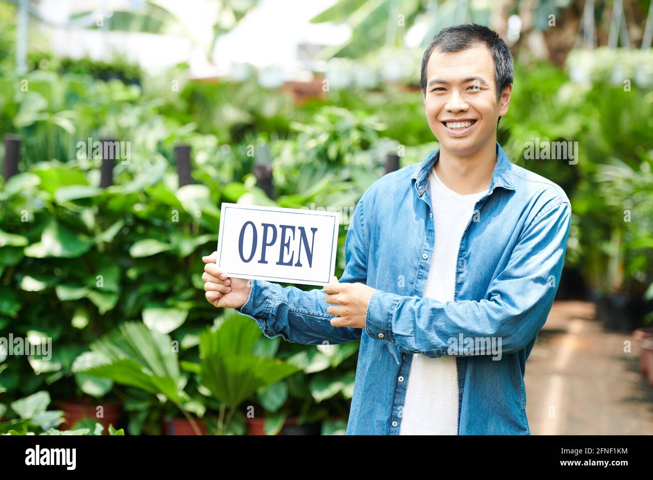 Ritratto di giovane sorridente che apre vivaio pianta e invitante clienti Foto Stock