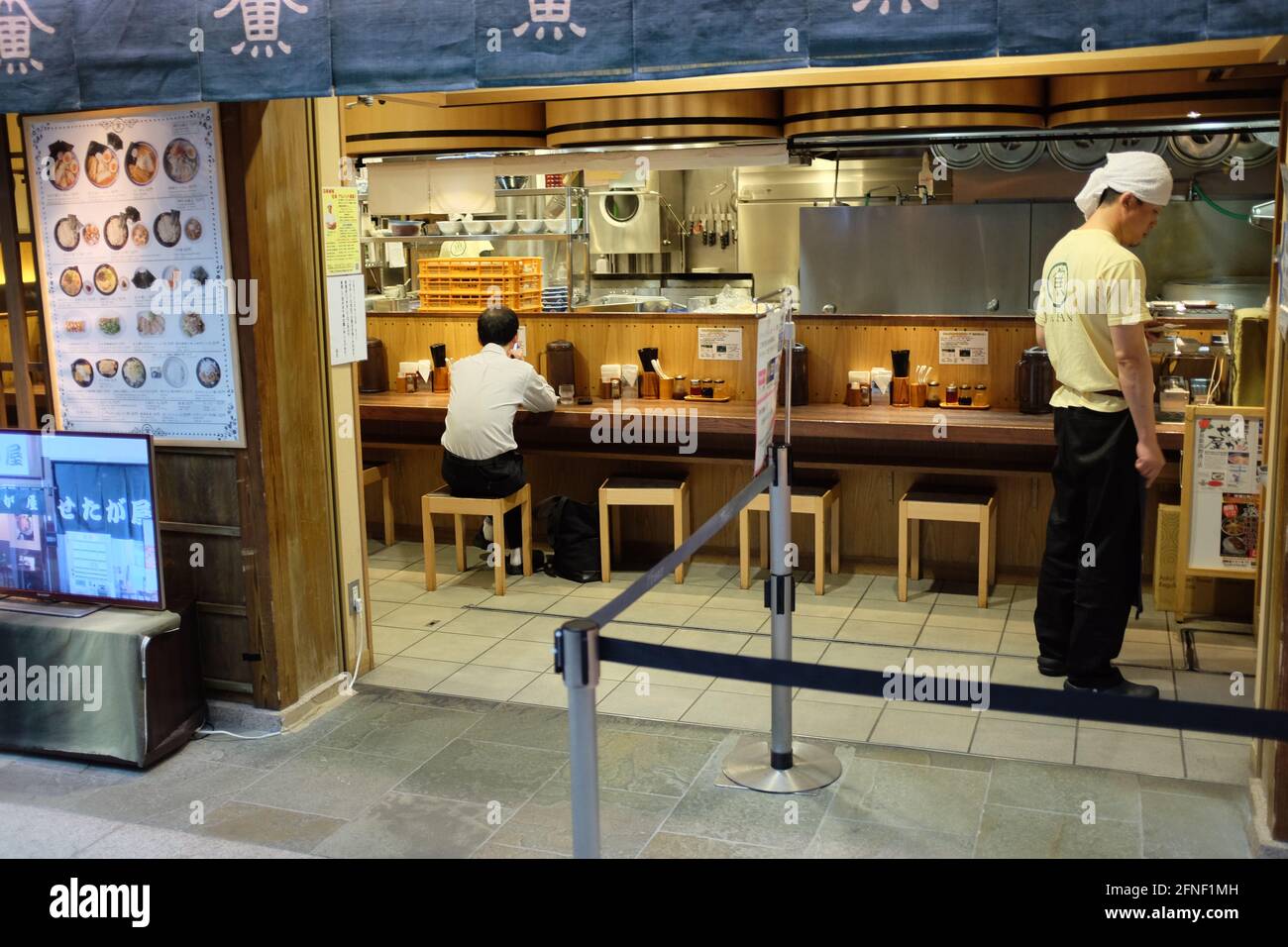 Un uomo d'affari giapponese siede in un ristorante Sushi bar mentre un dipendente frequenta il banco a Toykyo, Giappone Foto Stock