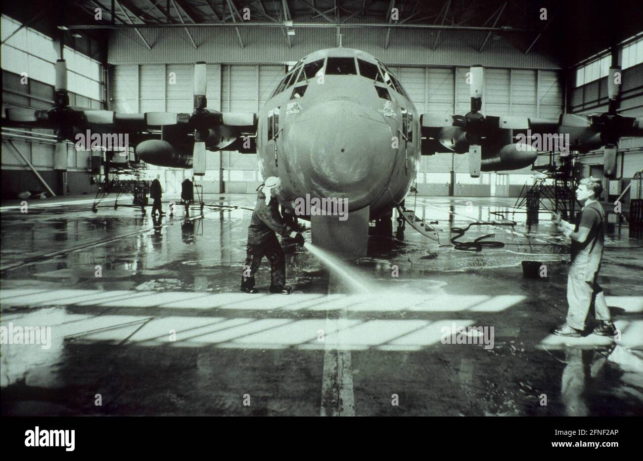 Soldati tubo giù il pavimento di un hangar dell'aeroplano. Sullo sfondo, un aereo di trasporto C-130 Hercules. [traduzione automatizzata] Foto Stock