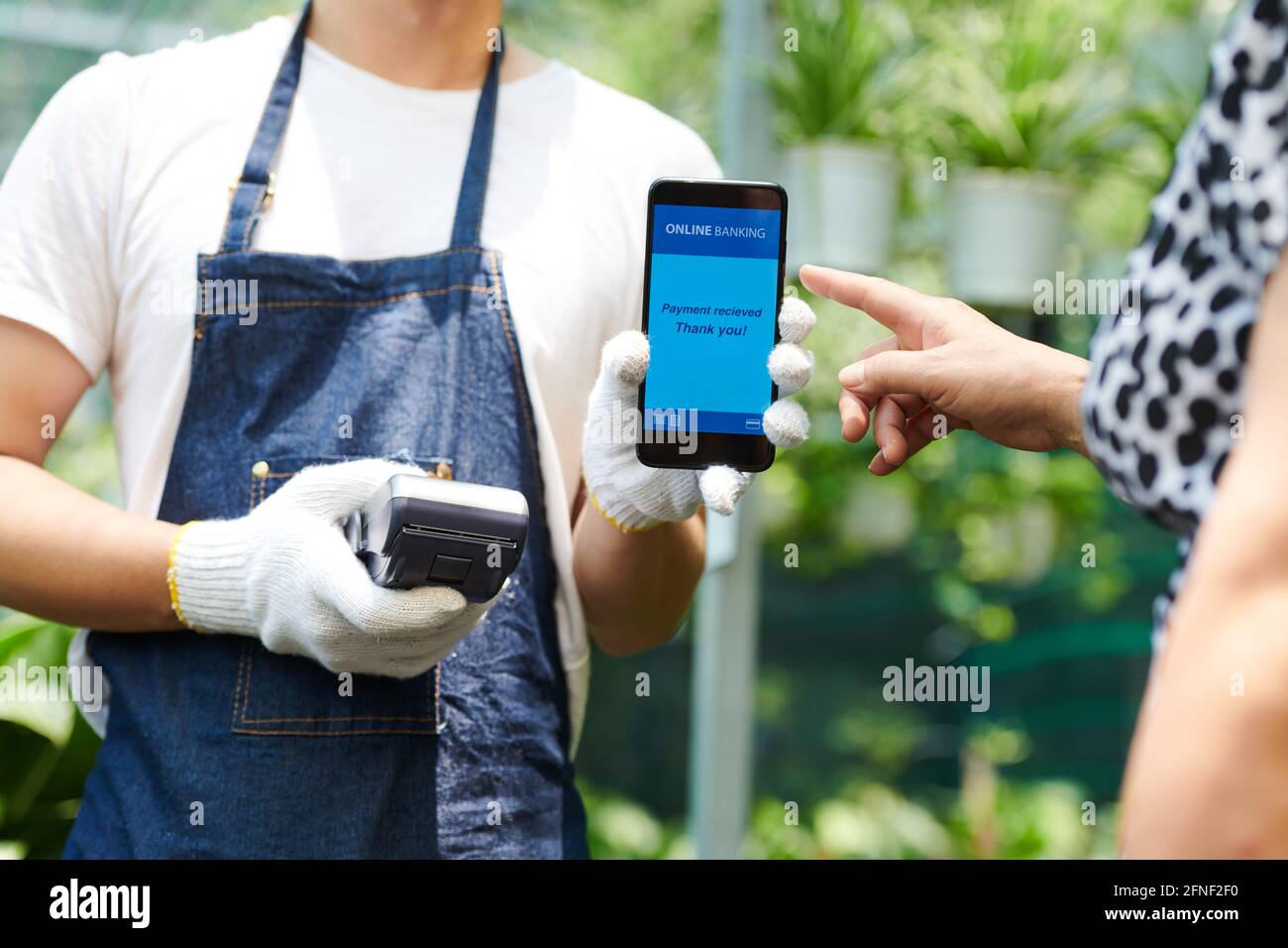 Serenatore in guanti protettivi che tengono teminale e accettando senza contatto Pagamento da parte del cliente tramite tecnologia NFC Foto Stock
