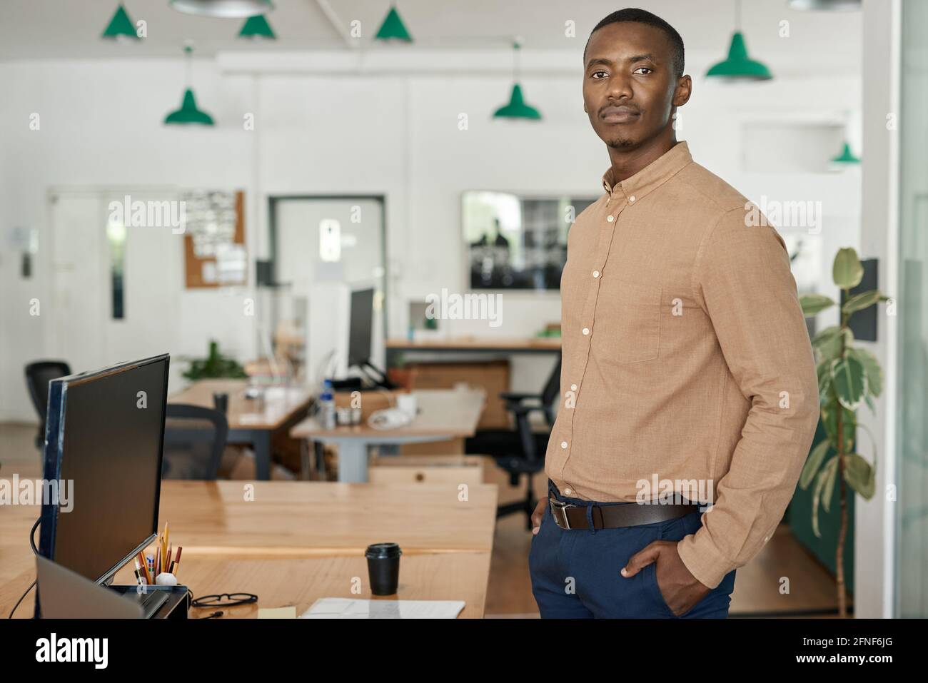 Giovane uomo d'affari africano sicuro che si trova da solo in un ufficio Foto Stock