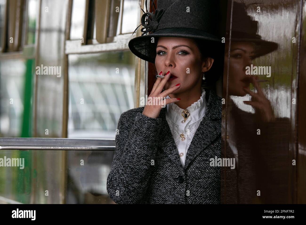 bella donna in costume vintage anni '20 fumando sigaretta mentre si parte treno alla stazione ferroviaria Foto Stock