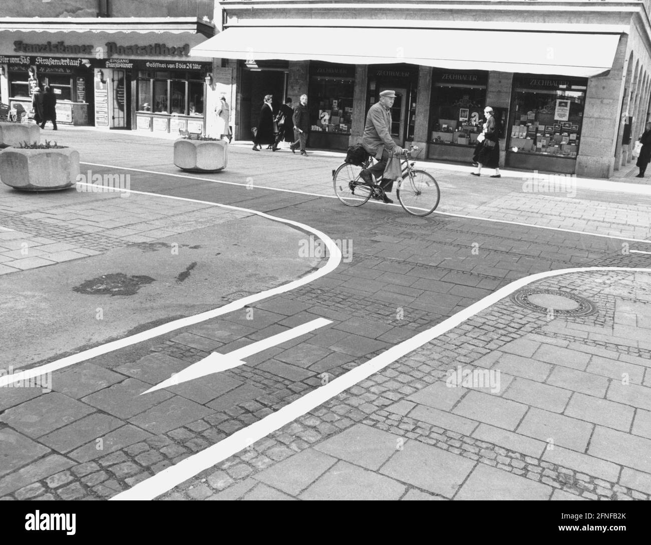 Un ciclista all'incrocio Residenz- Maximilianstraße su una pista ciclabile nera, che è stata separata dal sentiero pedonale da vasi di fiori. [traduzione automatizzata] Foto Stock