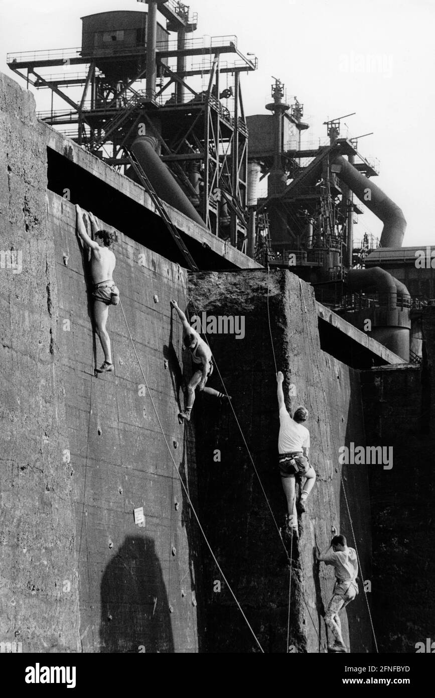 Vista degli altiforni in disuso delle acciaierie di Meiderich a Duisburg nel luglio 1991. In primo piano un gruppo di uomini salgono le pareti di arrampicata appena installate. Si trovano nei vecchi bunker di carbone, nelle aree di stoccaggio del carbone vicino agli altiforni. Le pareti di arrampicata sono state create nell'ambito della trasformazione della vecchia area industriale nel Parco paesaggistico di Duisburg-Nord. [traduzione automatizzata] Foto Stock