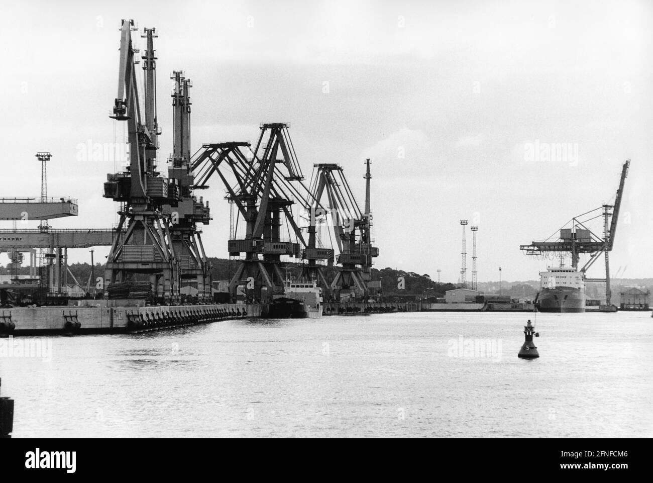 Nel cantiere Rostock si possono vedere le gru e sullo sfondo una nave che viene scaricata. Sul canale boe mostrare la strada. Il porto d'oltremare di Rostock è stato ampliato tra il 1957 e il 1960 e investito nell'industria dei cantieri navali. [traduzione automatizzata] Foto Stock