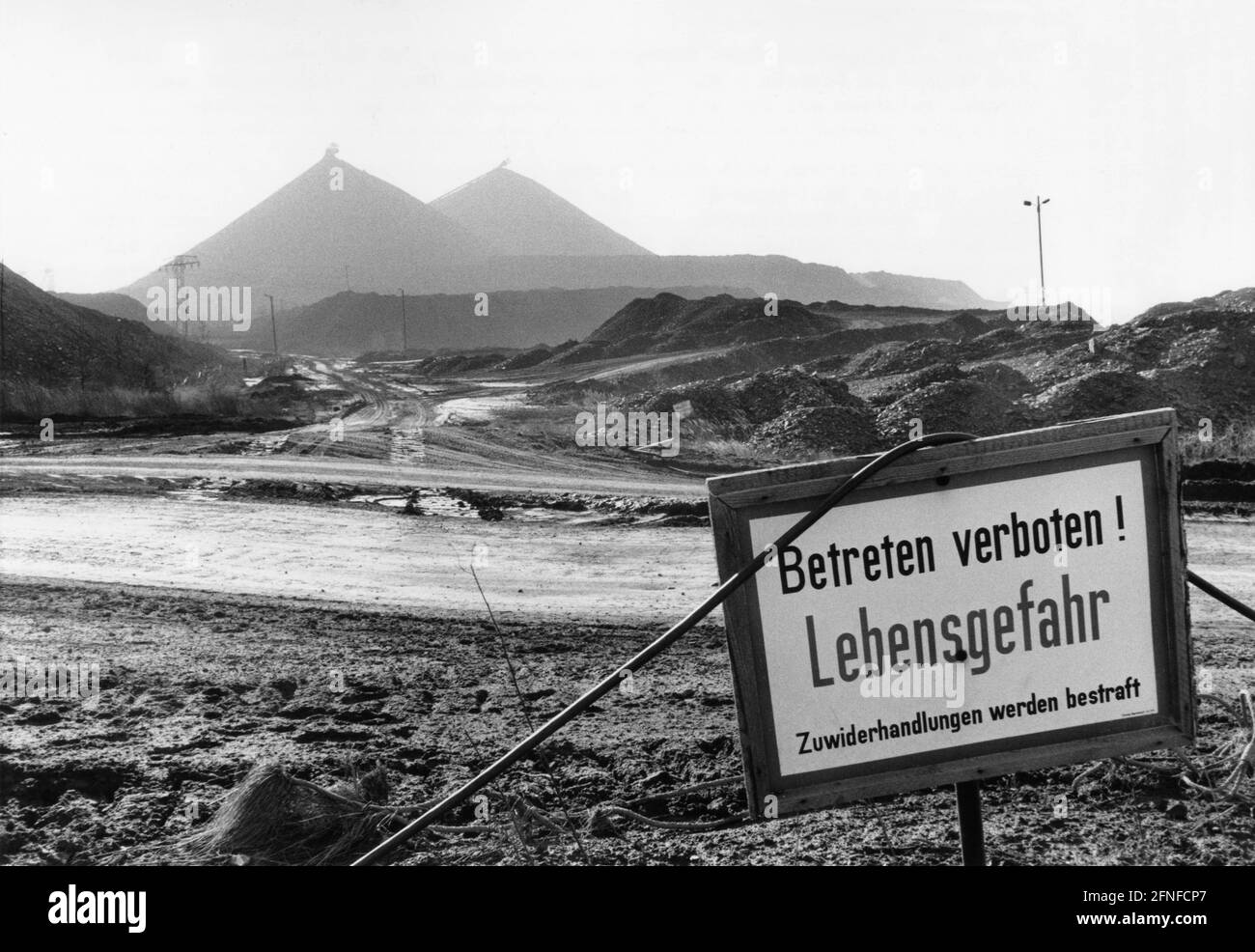 Alle spalle della città di Ronneburg sorgono i cumuli appuntiti di estrazione dell'uranio. La più grande area estrattiva di uranio in Europa si trova tra Gera e Karl-Marx-Stadt e sotto la gestione di SDAG, la società mista sovietico-tedesca. In primo piano è possibile vedere un segno di avvertimento contro l'ingresso nell'area. [traduzione automatizzata] Foto Stock