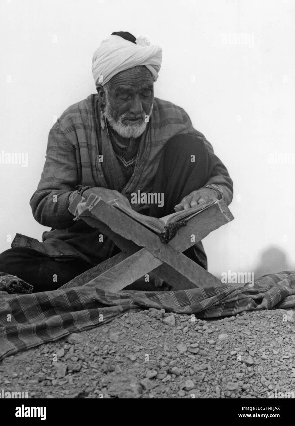 Un anziano studia il Corano nel deserto iraniano. La comunità religiosa musulmana continua a crescere, attribuibile in primo luogo alla crescita della popolazione in paesi prevalentemente musulmani e in secondo luogo alla crescente attrattiva dell'Islam dovuta all'aumento degli arabi attraverso il petrolio. [traduzione automatizzata] Foto Stock