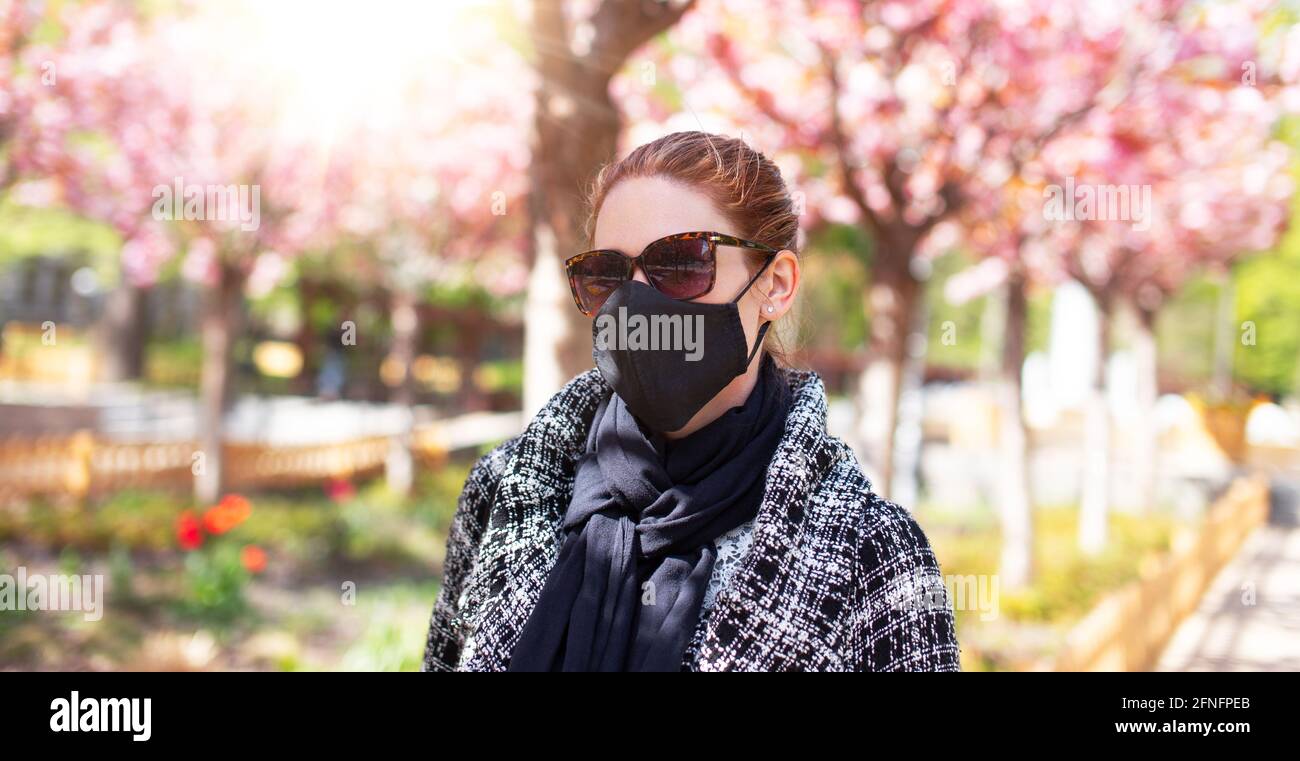 Giovane donna rossa in maschera nera al parco durante Sakura, covid-19 Foto Stock