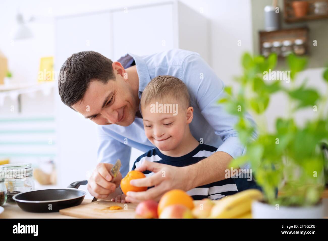 Padre con il figlio della sindrome di Happy Down all'interno della cucina, preparando il cibo. Foto Stock