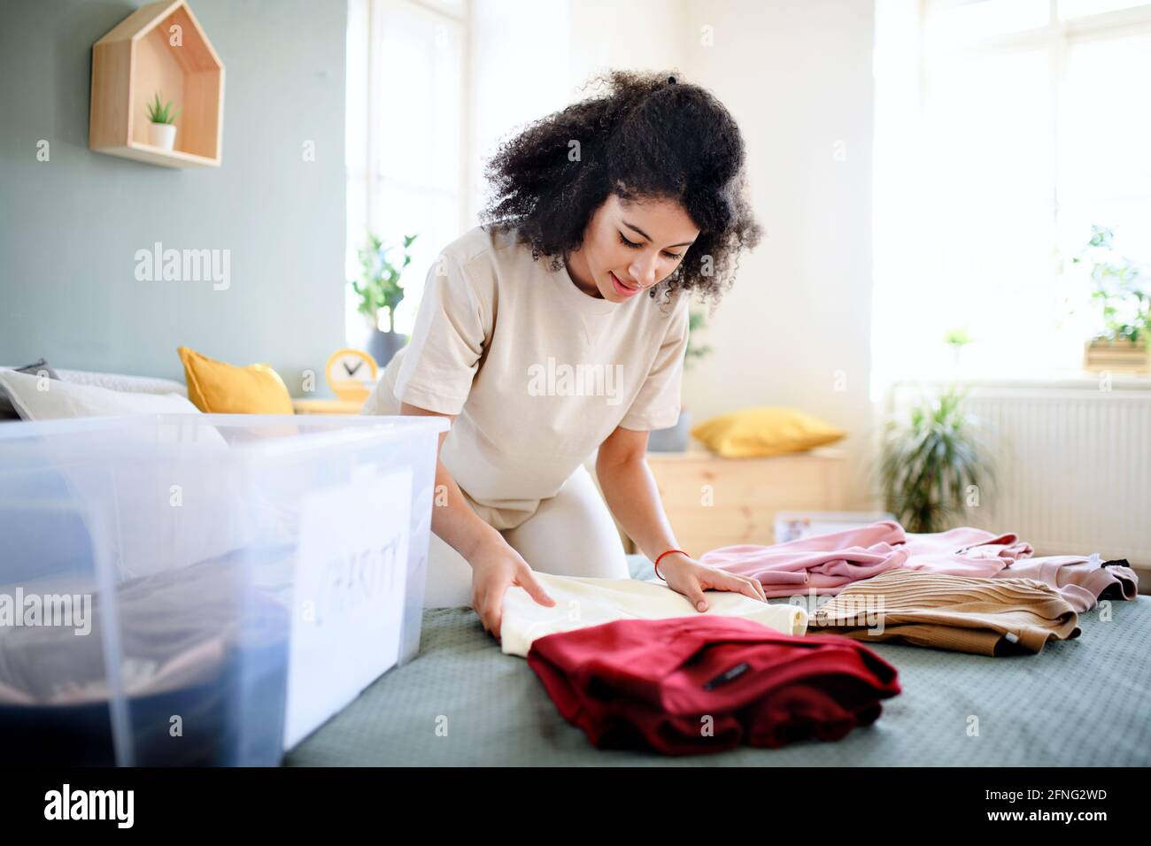 Giovane donna di smistamento guardaroba interno a casa, donazione di beneficenza concetto. Foto Stock