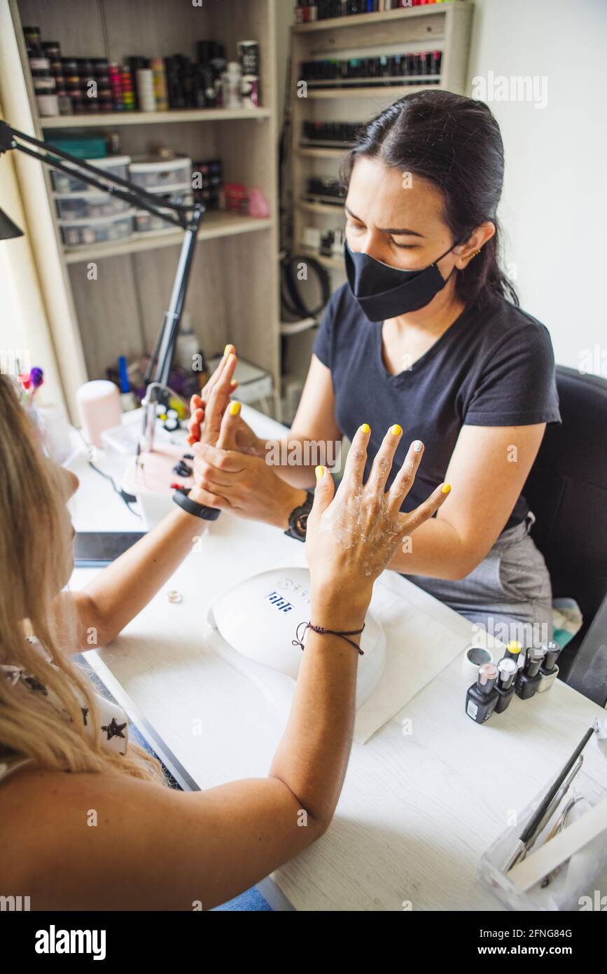 manicurista massaggiare le mani del cliente senza volto dopo l'applicazione di olio cosmetico in studio unghie Foto Stock