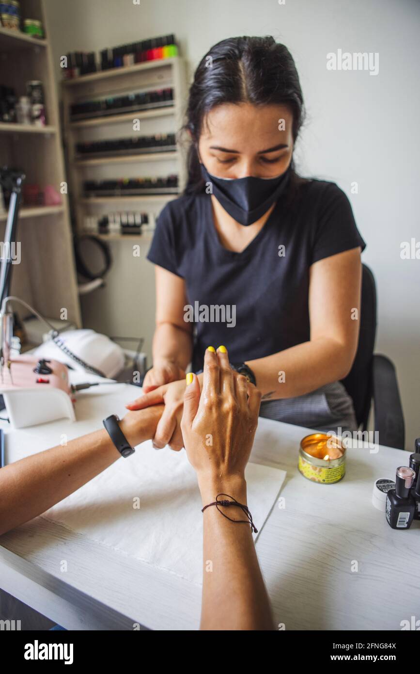 manicurista massaggiare le mani del cliente senza volto dopo l'applicazione di olio cosmetico in studio unghie Foto Stock