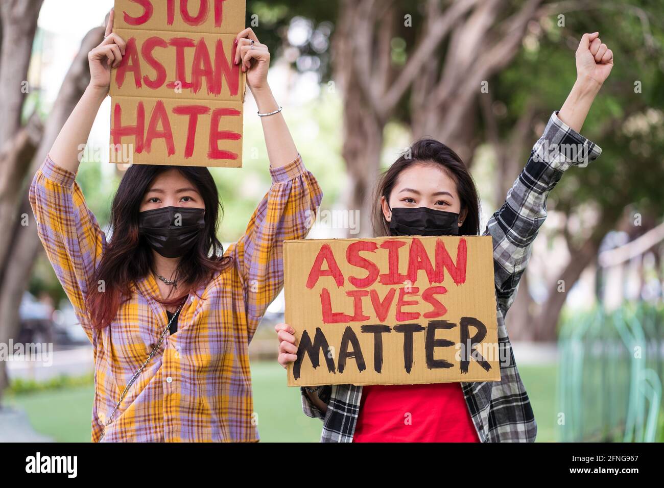 Femmine etniche in maschere e con Stop odio asiatico e. Le vite asiatiche manifestano la materia protestando contro il razzismo in città e guardando la fotocamera Foto Stock