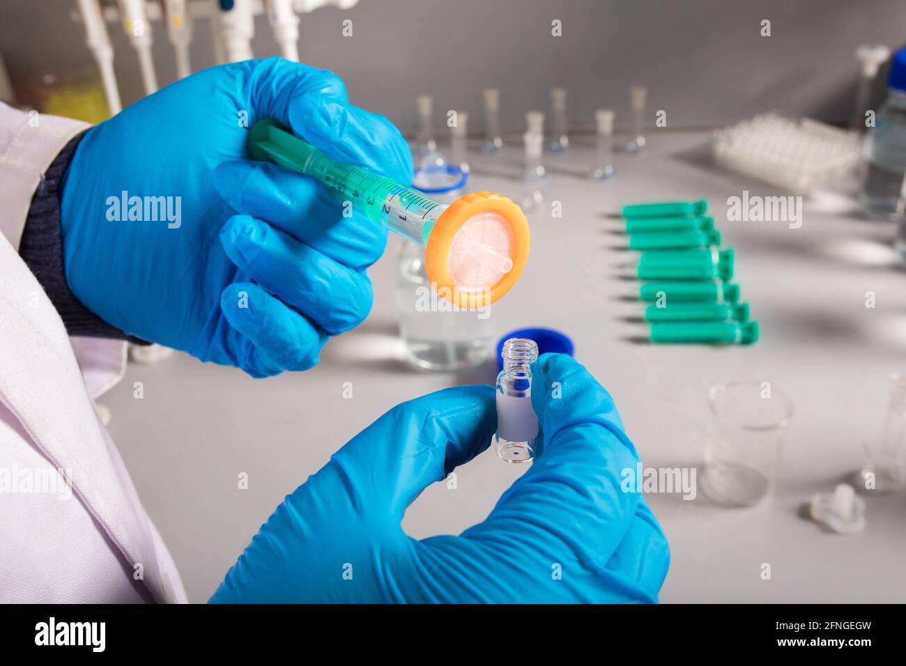 Coltivare biologo irriconoscibile in guanti in lattice riempiendo l'iniettore con liquido da un piccolo flacone in laboratorio Foto Stock