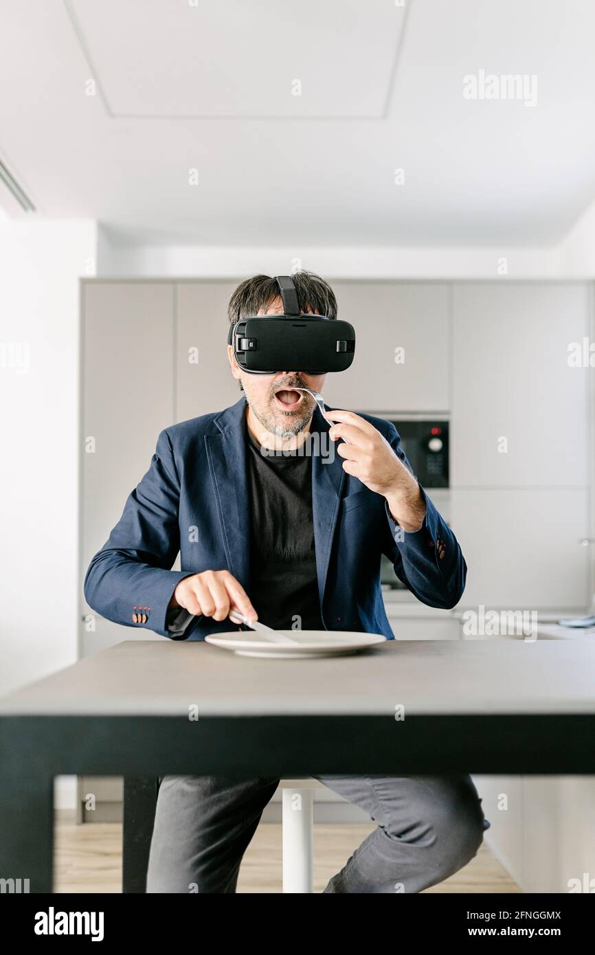 Elegante uomo adulto che finge di mangiare in una cucina moderna sperimentando la realtà virtuale sul piatto vuoto. Occhiali per realtà virtuale. Cibo virtuale, grazie Foto Stock