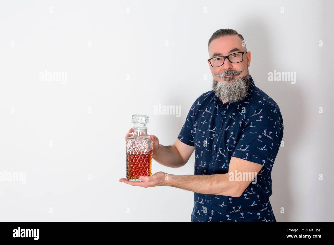 Hipster retro look con barba grande e bicchieri, 40-45 anni, caucasico, tenendo vecchia bottiglia di liquore e guardando dritto. Foto Stock