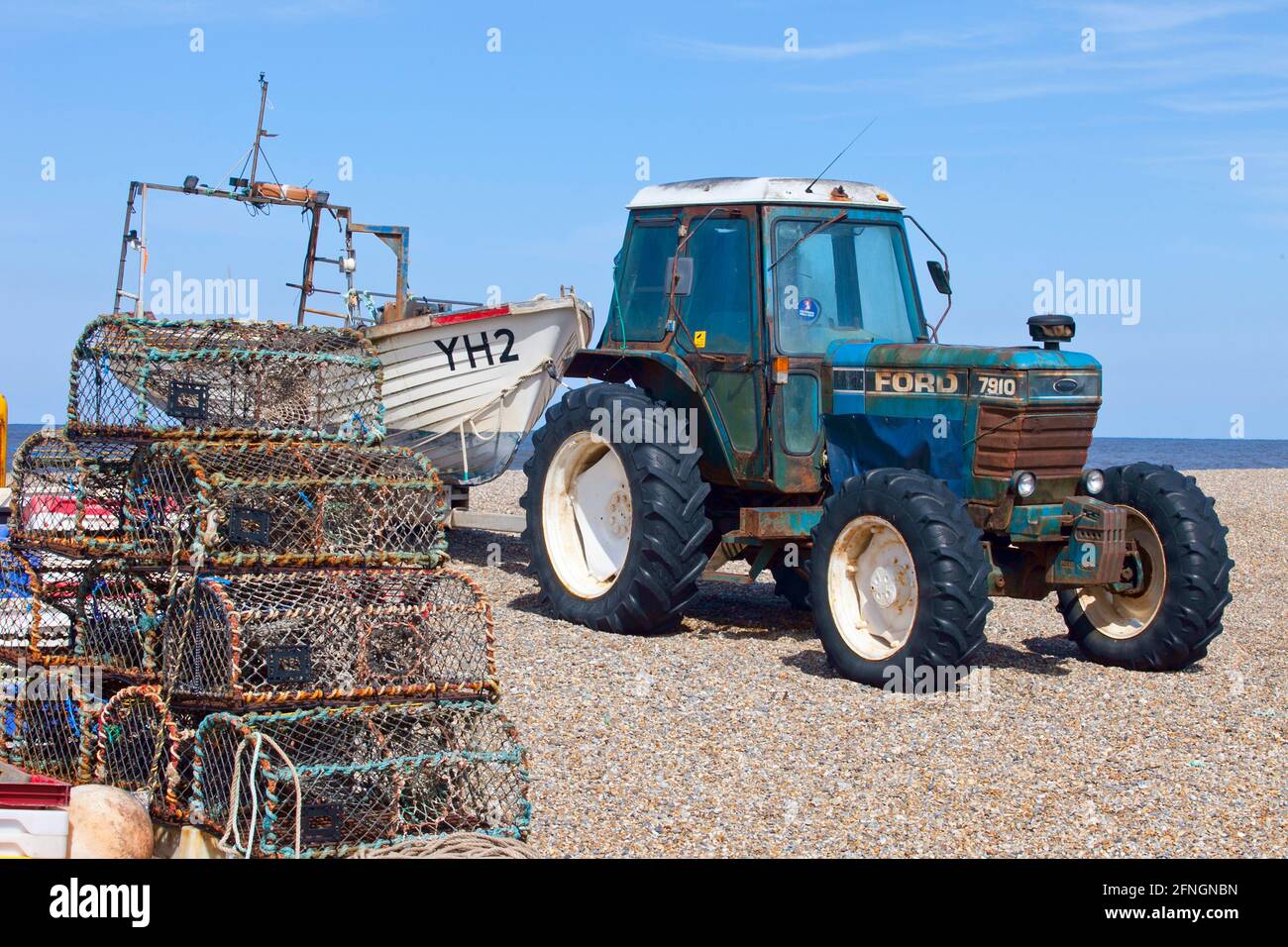 Pentole di aragosta sulla spiaggia di ciottoli con trattore ford e barca da pesca Foto Stock