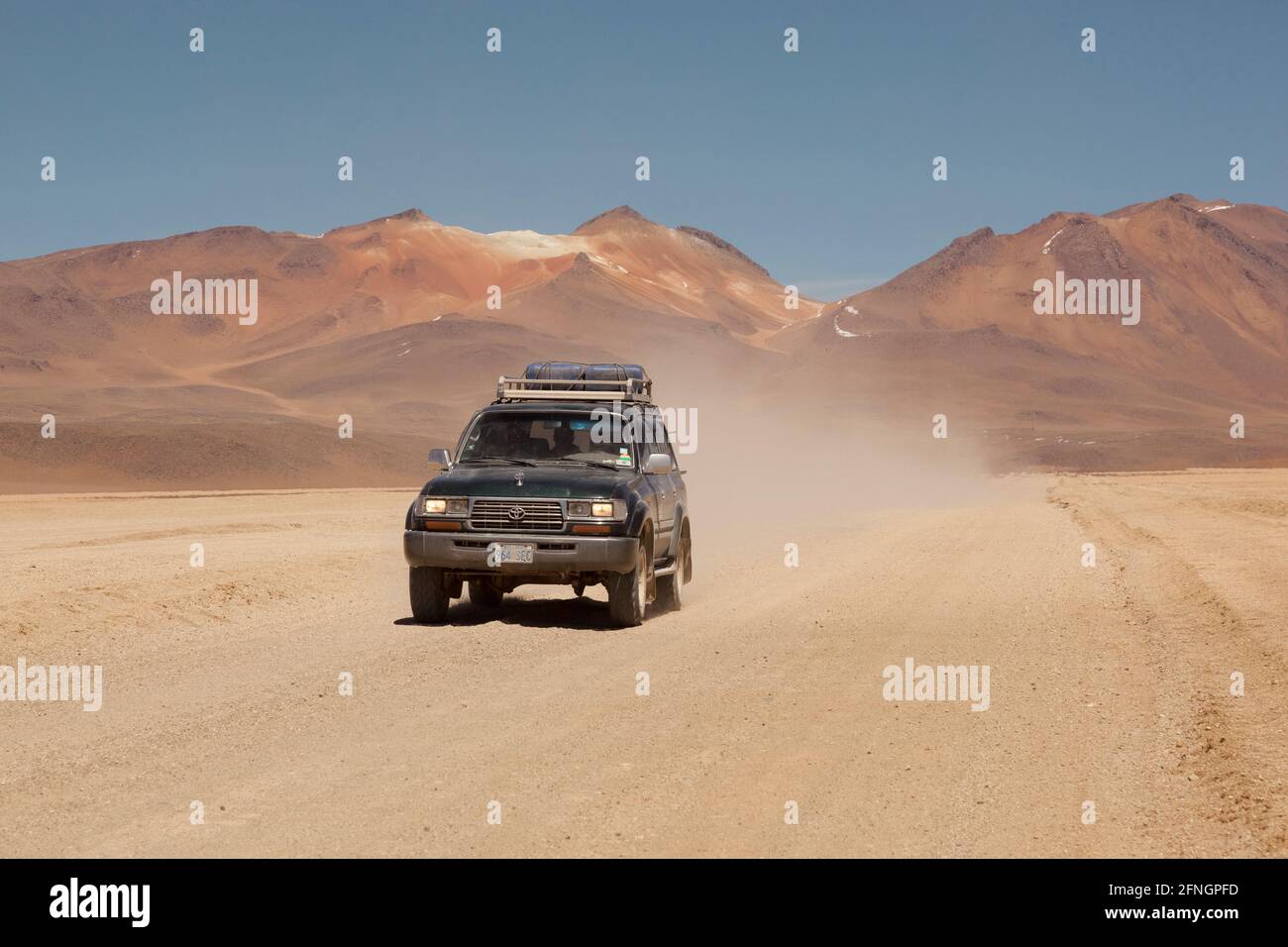 Sullo sfondo di vulcani, un veicolo fuoristrada 4x4 attraversa il paesaggio desertico della Bolivia in un safari turistico terrestre. Foto Stock