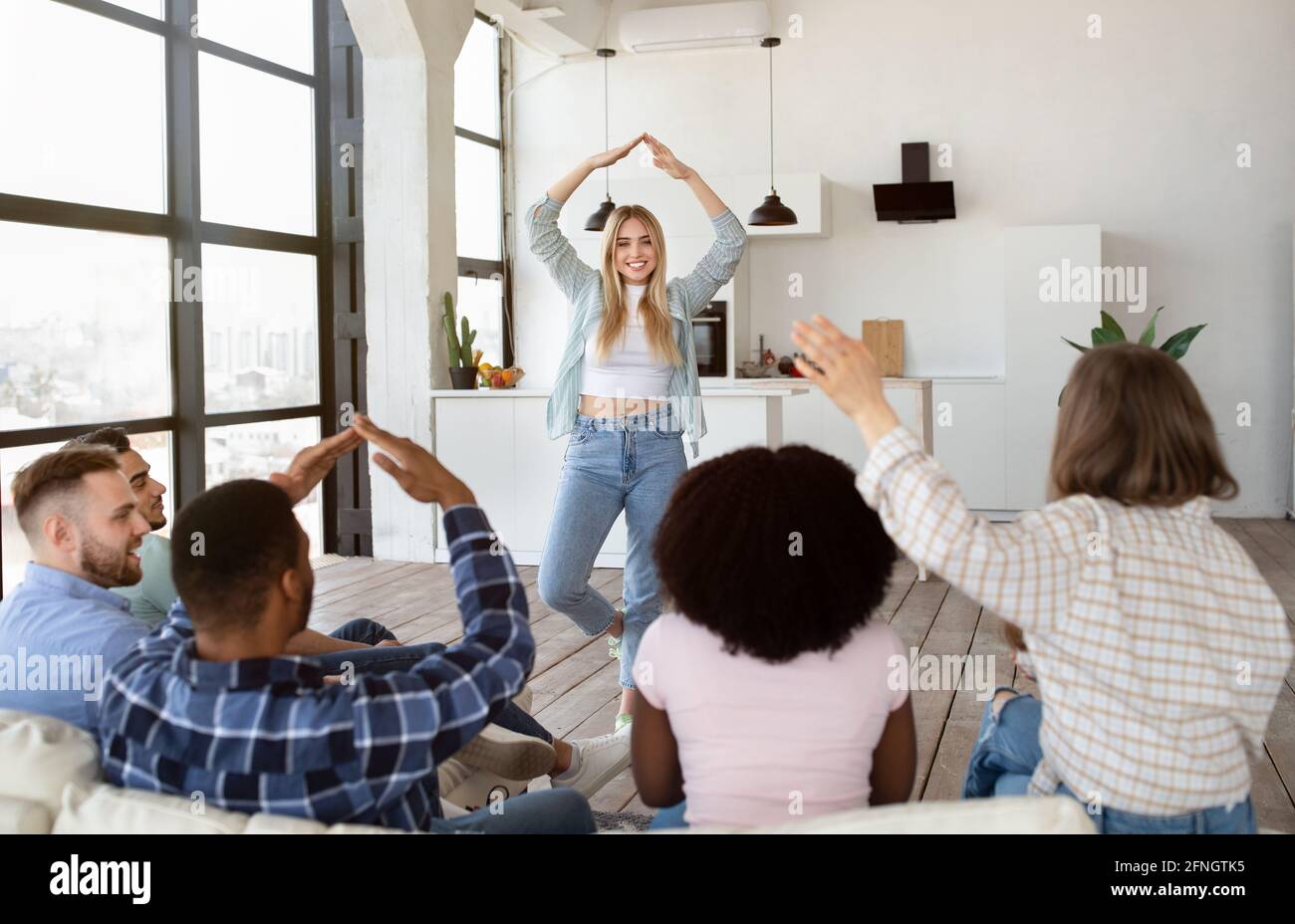 Gruppo di amici allegri e diversi che giocano a Charades indovinare gioco a. casa Foto Stock