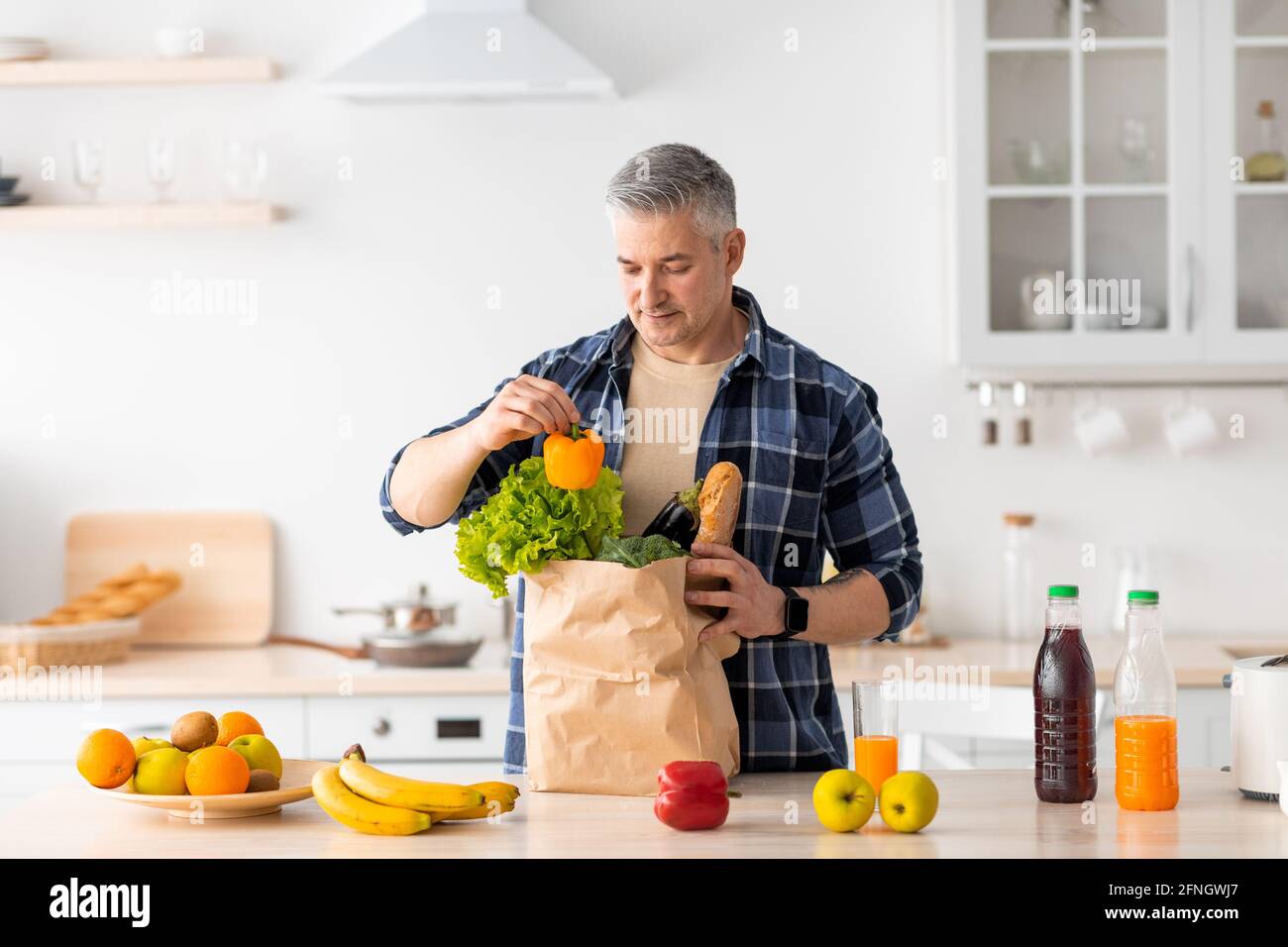 Concetto di consegna degli alimenti. Uomo anziano felice che disimballo la borsa di carta con la drogheria ordinata da internet Foto Stock
