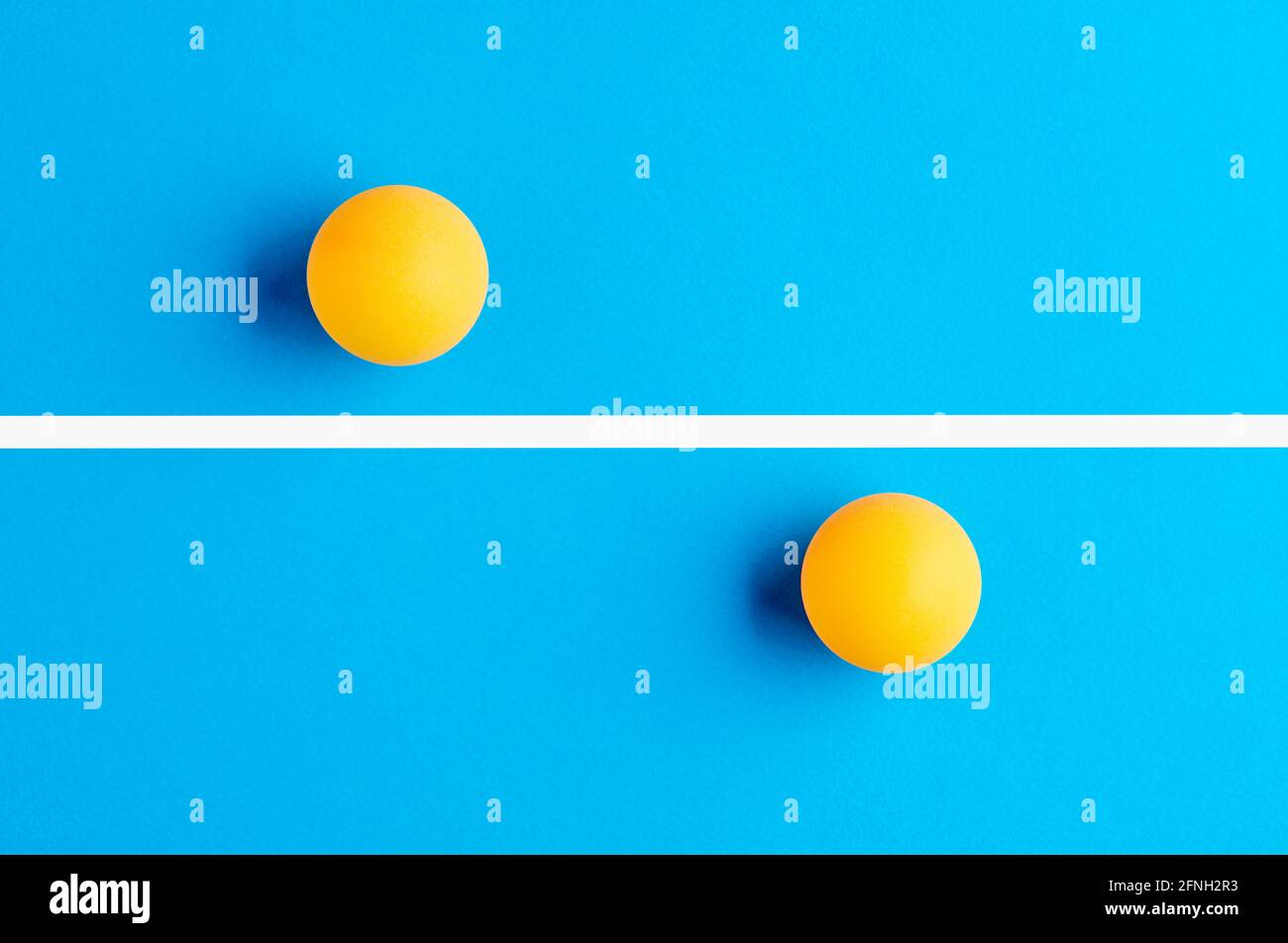 Due palline da ping-pong arancioni sono contrapposte, divise da una linea su sfondo blu. Concetto di concorrenza. Foto Stock