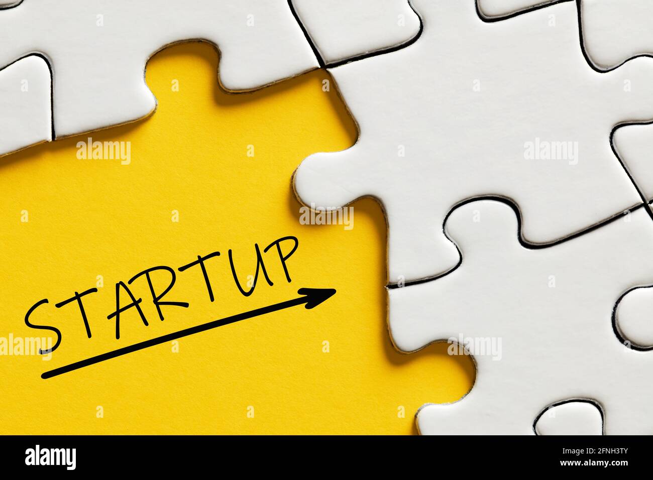La parola startup su sfondo giallo circondato da pezzi di puzzle. Concetto di avvio aziendale o aziendale. Foto Stock