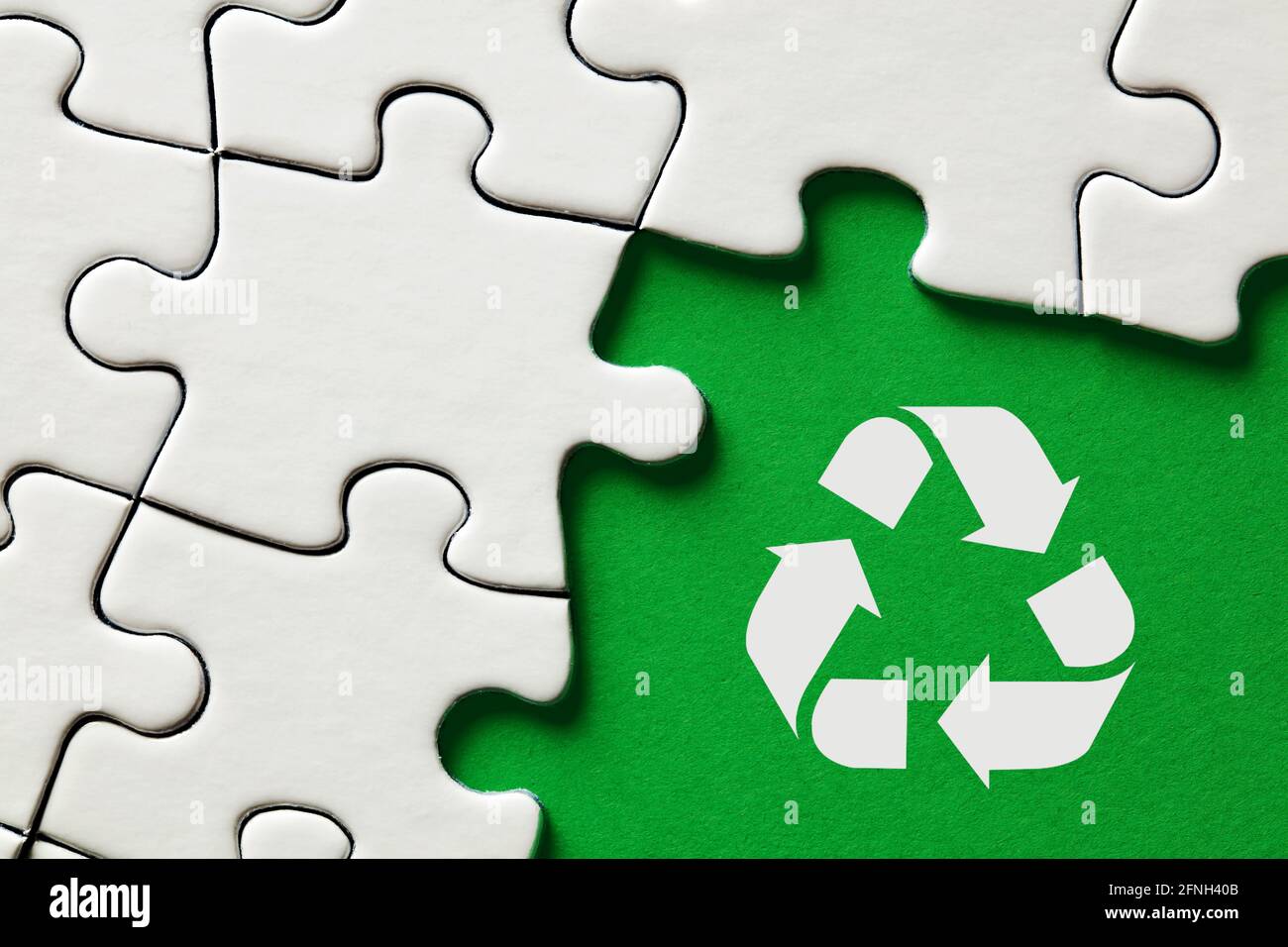 Icona di riciclaggio su sfondo verde circondata da pezzi di puzzle. Riciclare per il concetto di conservazione ambientale. Foto Stock