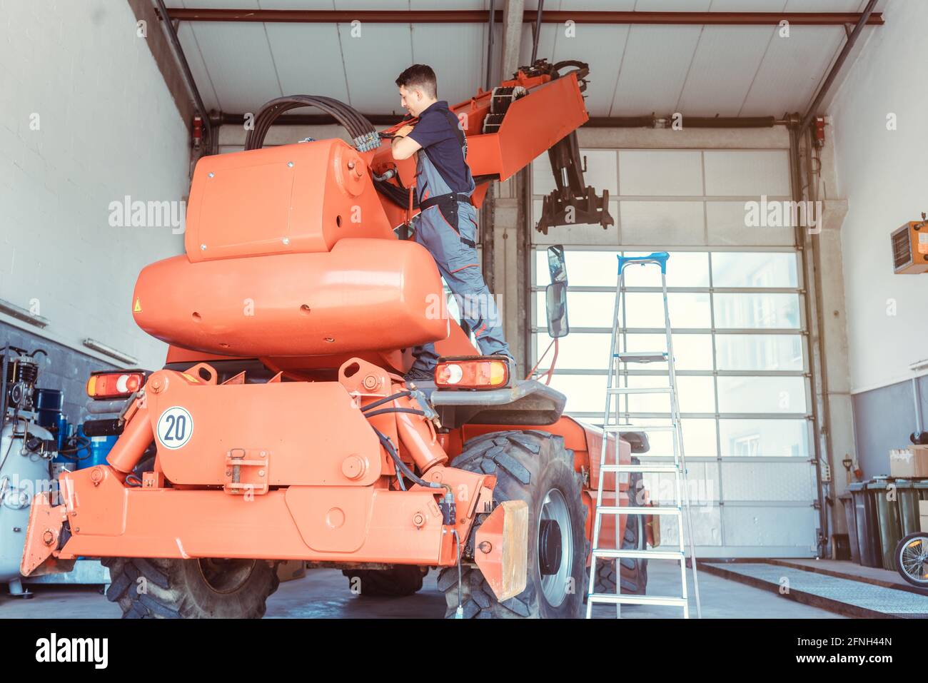 Machinista che ripara una macchina agricola enorme nel suo garage Foto Stock