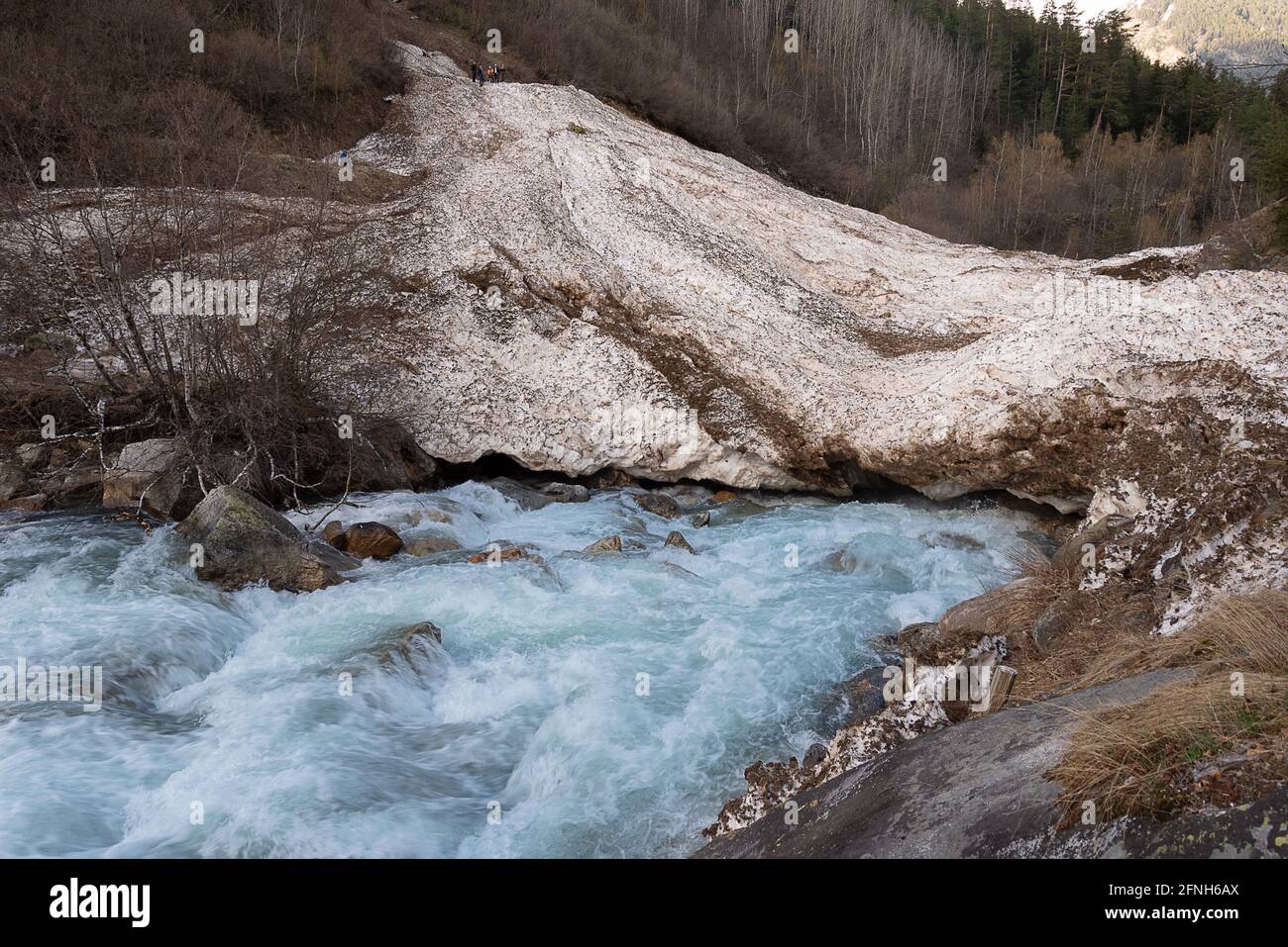 un fiume di montagna scorre sotto una valanga con la gente a. la parte superiore Foto Stock