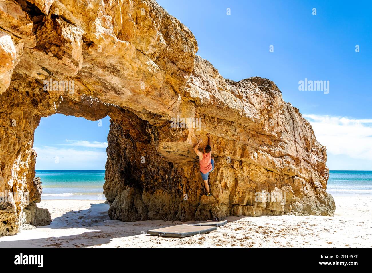 Giovane scalatore di roccia salendo in modo sicuro una scogliera gialla ad Algarve, Portogallo Foto Stock