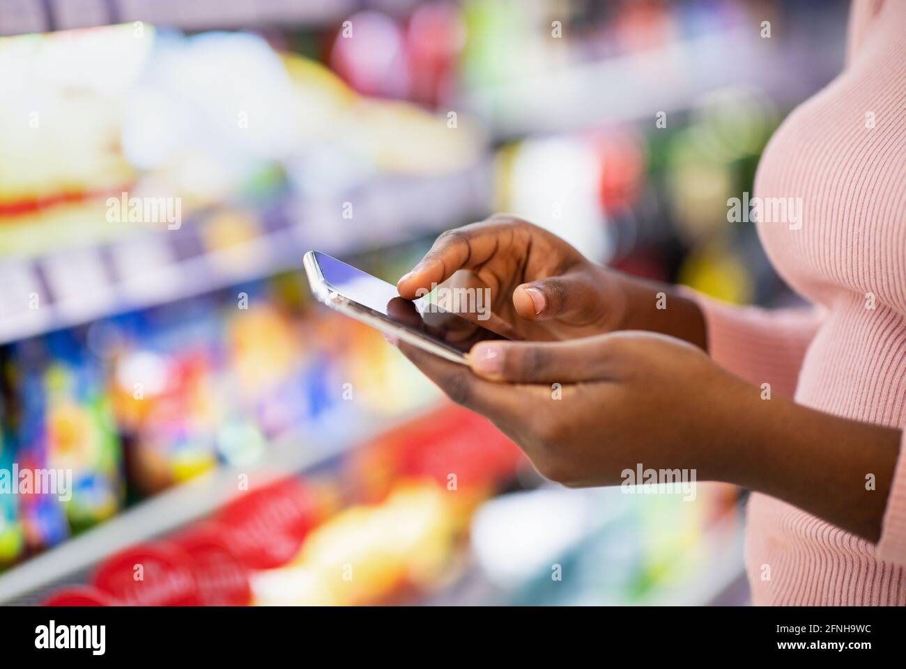 Vista ritagliata di giovane donna nera che controlla l'app della lista della spesa sul cellulare al supermercato, spazio di copia Foto Stock
