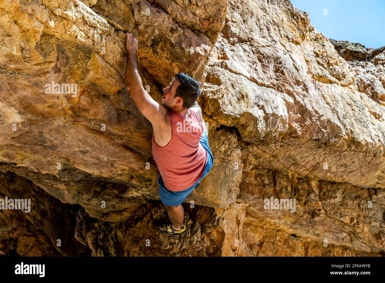 Giovane scalatore di roccia salendo in modo sicuro una scogliera gialla ad Algarve, Portogallo Foto Stock