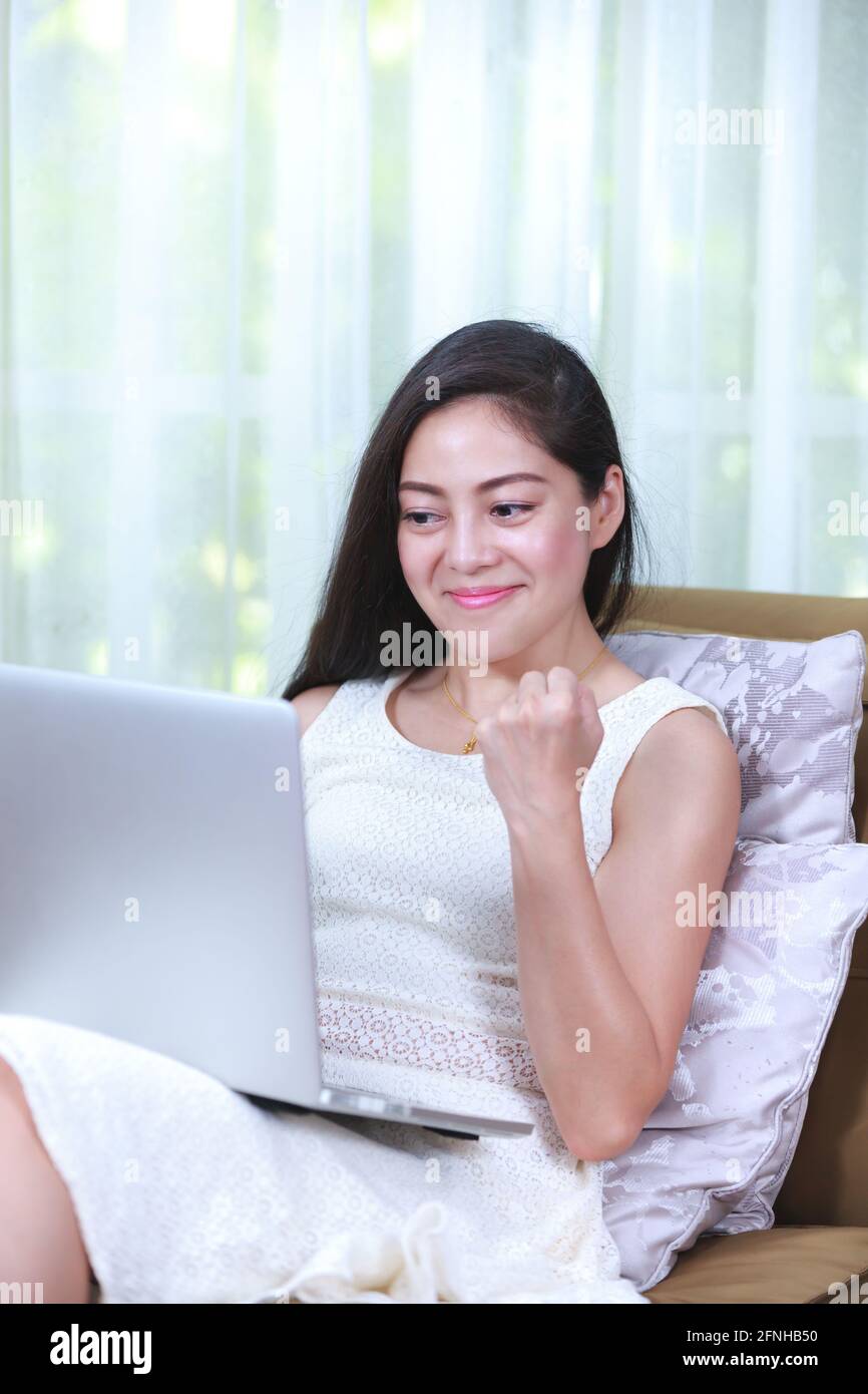 Bella donna d'affari asiatica che lavora da casa con il computer portatile per ottenere tutto il suo business. Emozione umana positiva. Azione del vincitore o peop riuscito Foto Stock